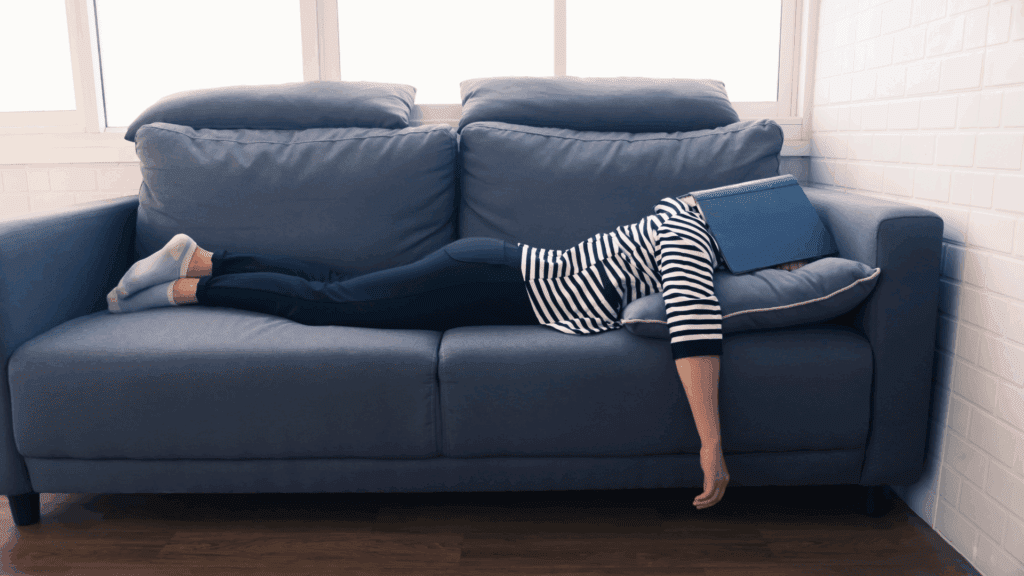 Person lying on a couch with a book covering their face, representing avoidance behavior.