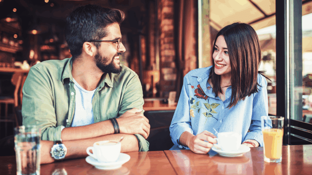 A couple smiling and enjoying a conversation over coffee.
