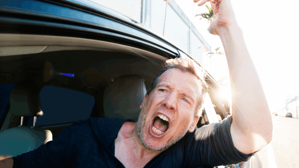 A frustrated man yelling out of a car window, illustrating road rage and reactive anger.