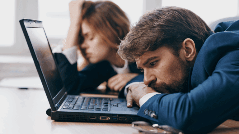 Two employees feeling underappreciated at work, sitting at a desk with slumped postures and a laptop in front of them.