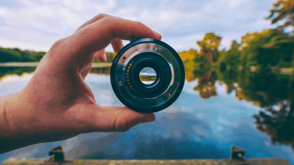Hand holding camera lens over lake, symbolizing focus in the neuroscience of perspective