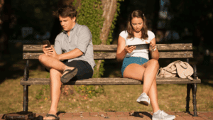 Couple sitting on a park bench distracted by phones, illustrating reward loops in digital behavior.
