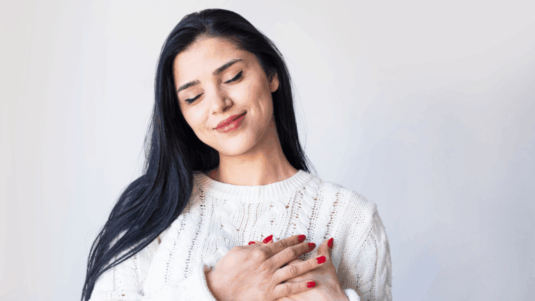 Woman smiling with eyes closed and hands on chest, expressing peace and connection with her authentic self.