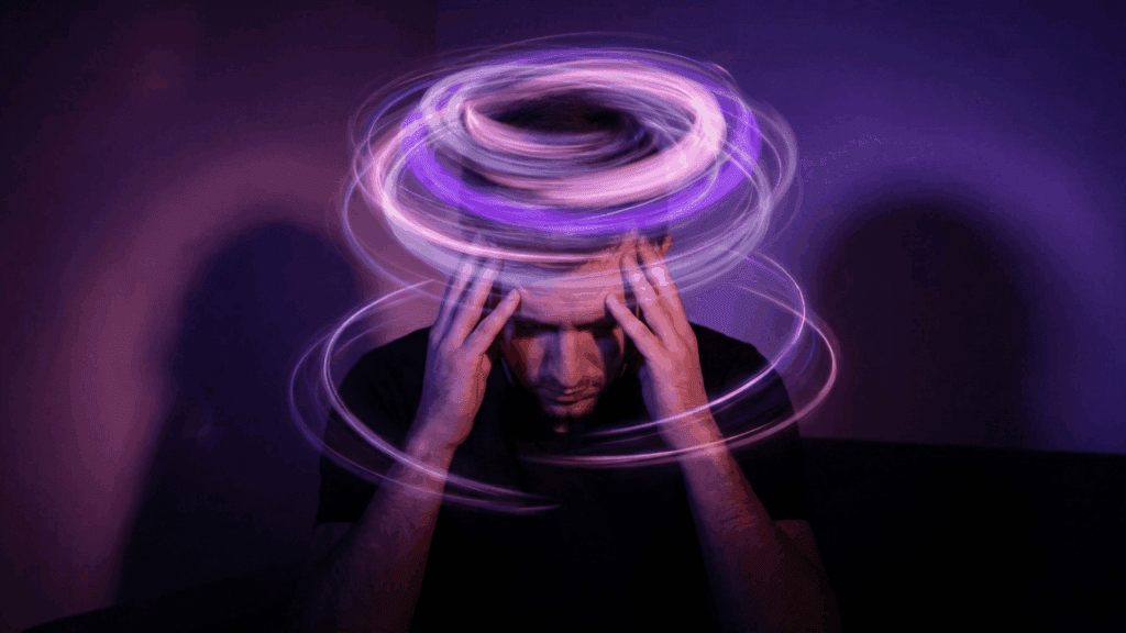 A man holds his head as glowing purple light trails spiral around his mind, representing the neuroscience of rumination.nnnn