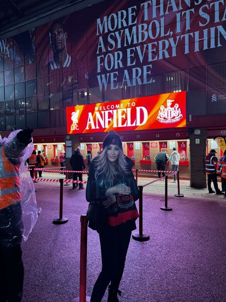 Dr. Sydney Ceruto posing in front of the Welcome to Anfield sign at Liverpool Football Club stadium on match day