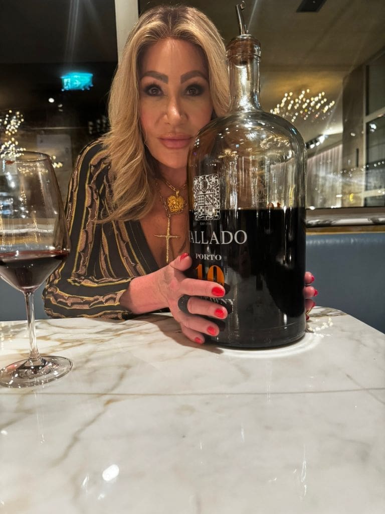 Dr. Sydney Ceruto seated at an elegant marble table holding a large Jeroboam bottle of Vallado Porto wine